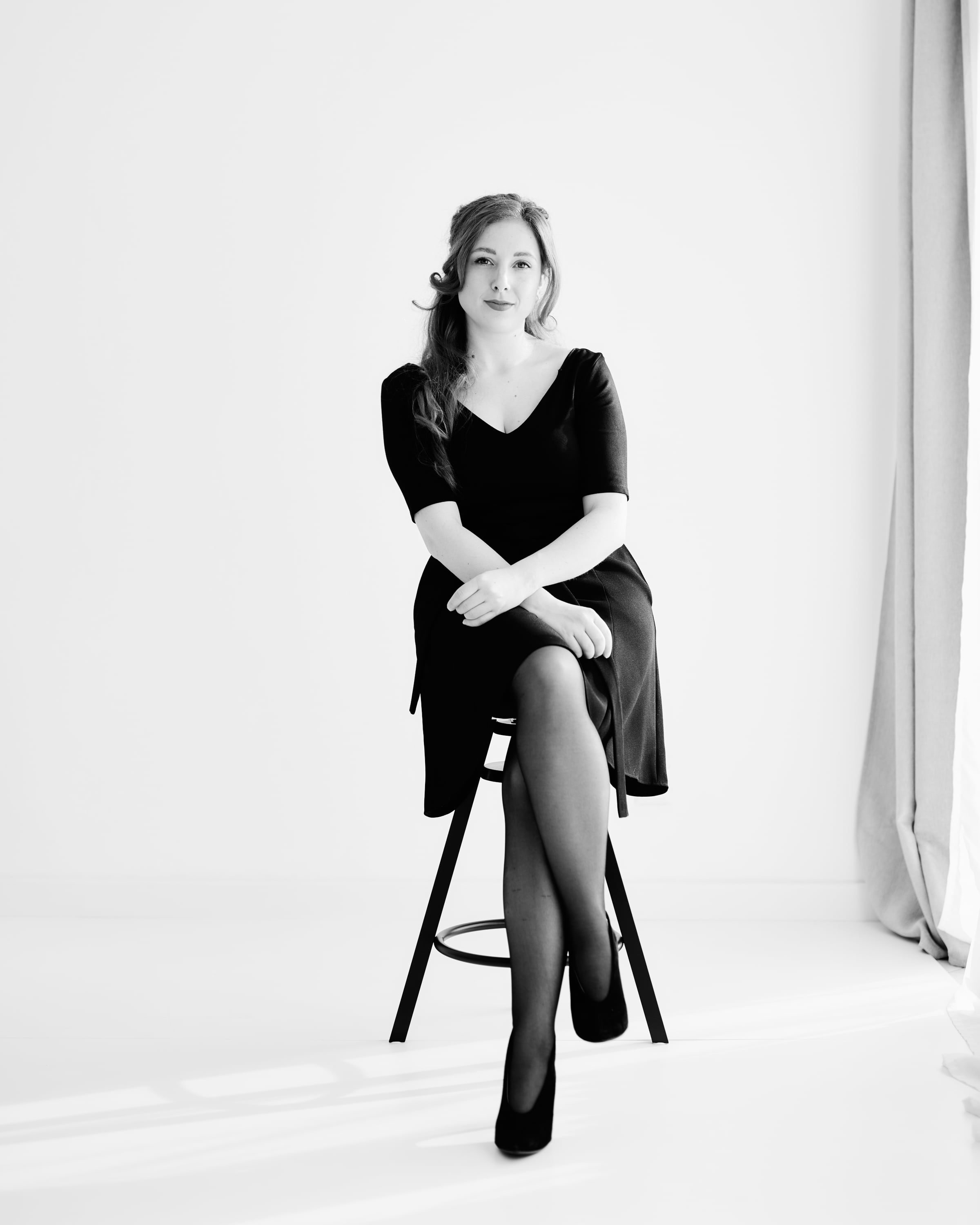 Schwarz-weißes Studioporträt von Christina Tschernitz, sitzend, im schwarzen Kleid